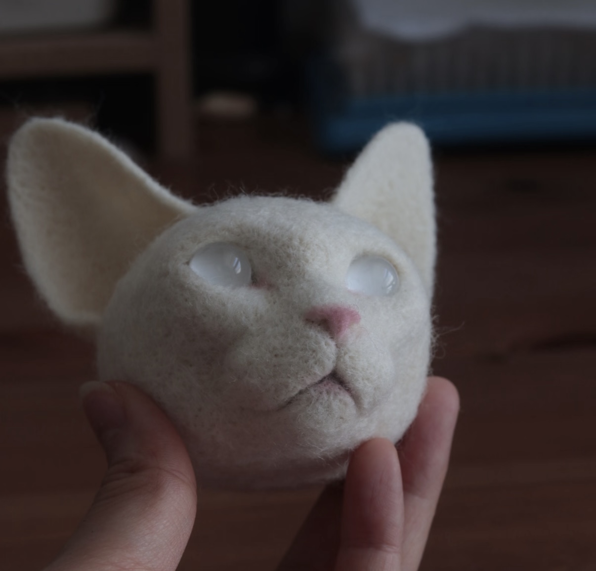 Unfinished felted cat head held in hand, showing the sculpted base form