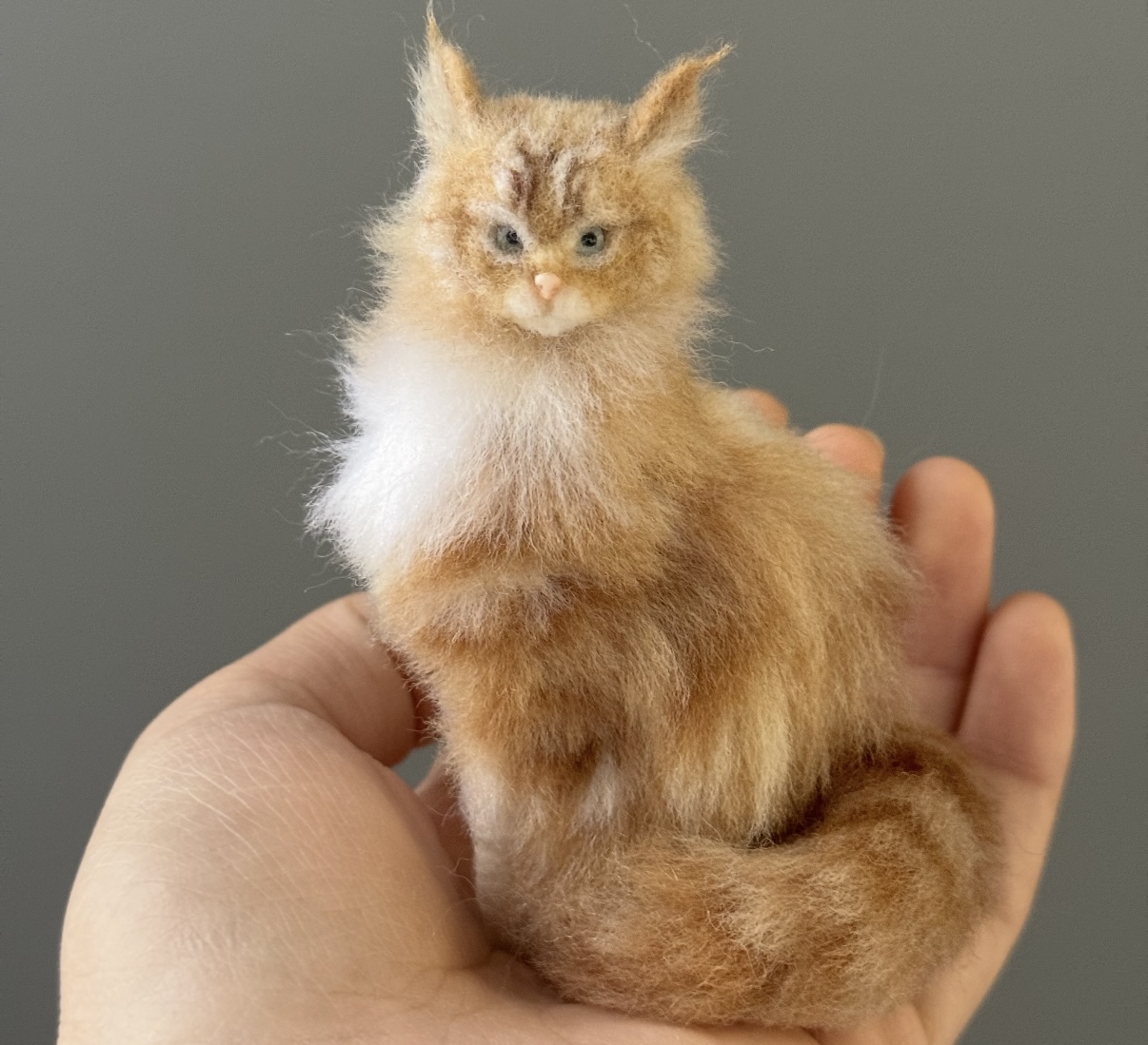Small ginger wool cat sculpture resting in the artist's palm