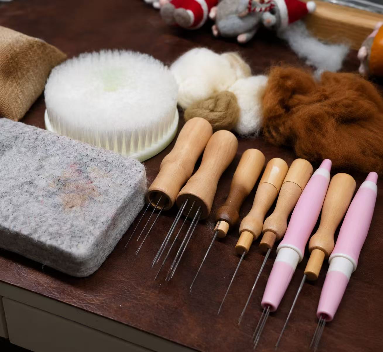 Felting needles, wool fibre and studio tools laid out on a workbench